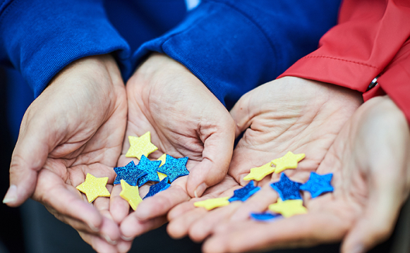 Hands holding stars in blue and yellow, the same colours of the EU flag