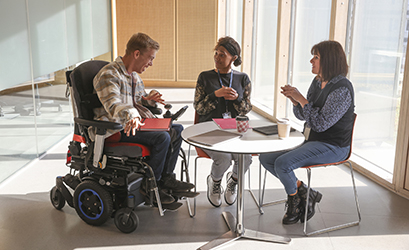Picture showing a group of colleagues around a table - one of the colleague is in a wheel chair (a man)