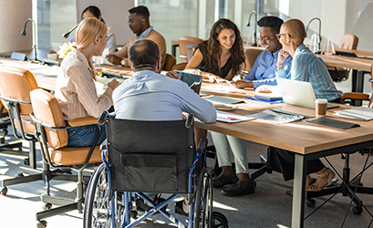 Picture showing a group of colleagues around a table - one of the colleague is in a wheel chair (a man)